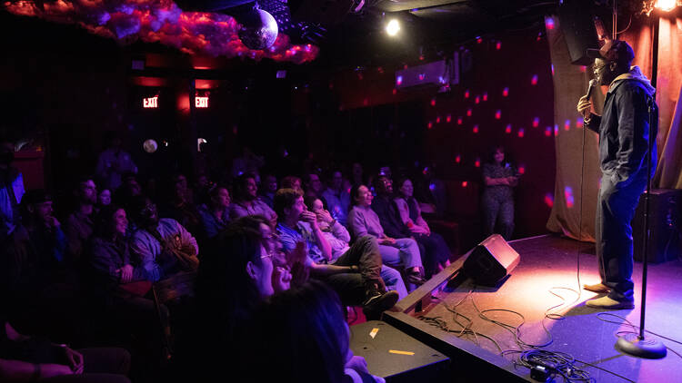 A comedian performing on stage in front of a seated audience A comedian performing on stage in front of a seated audience