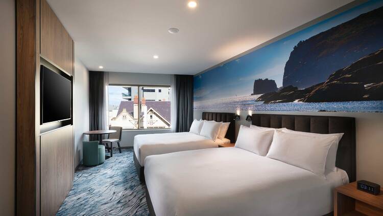 A hotel room with two queen beds and a mural of coastline on the wall