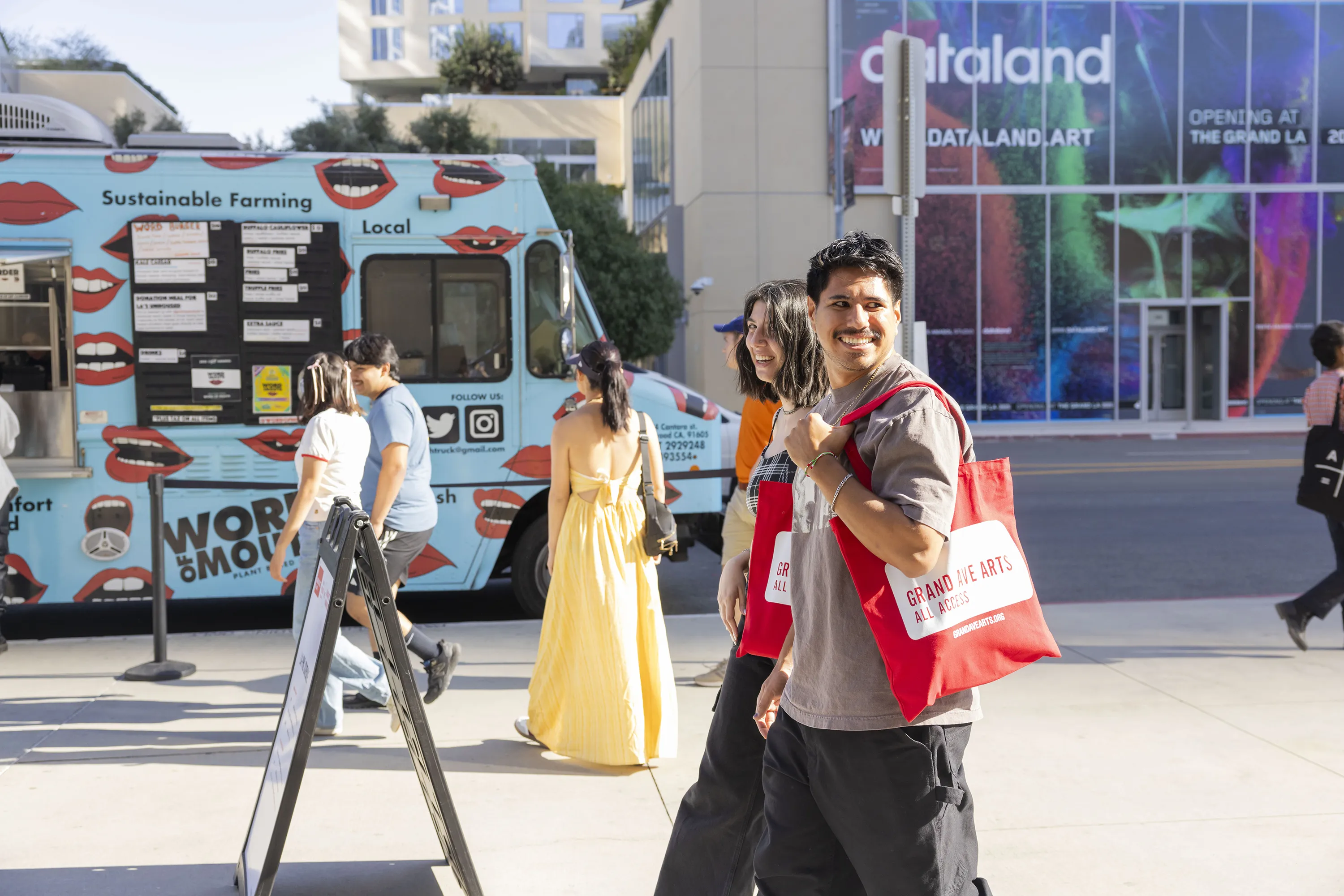 A man and woman carrying Grand Ave Arts: All Access tote bags walk by the Dataland space.