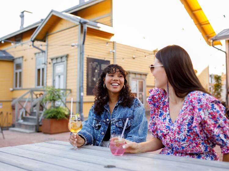 Two people enjoying drinks at Toivola Old Courtyard in Jyväskylä, seated outside a charming yellow building. Two people enjoying drinks at Toivola Old Courtyard in Jyväskylä, seated outside a charming yellow building.