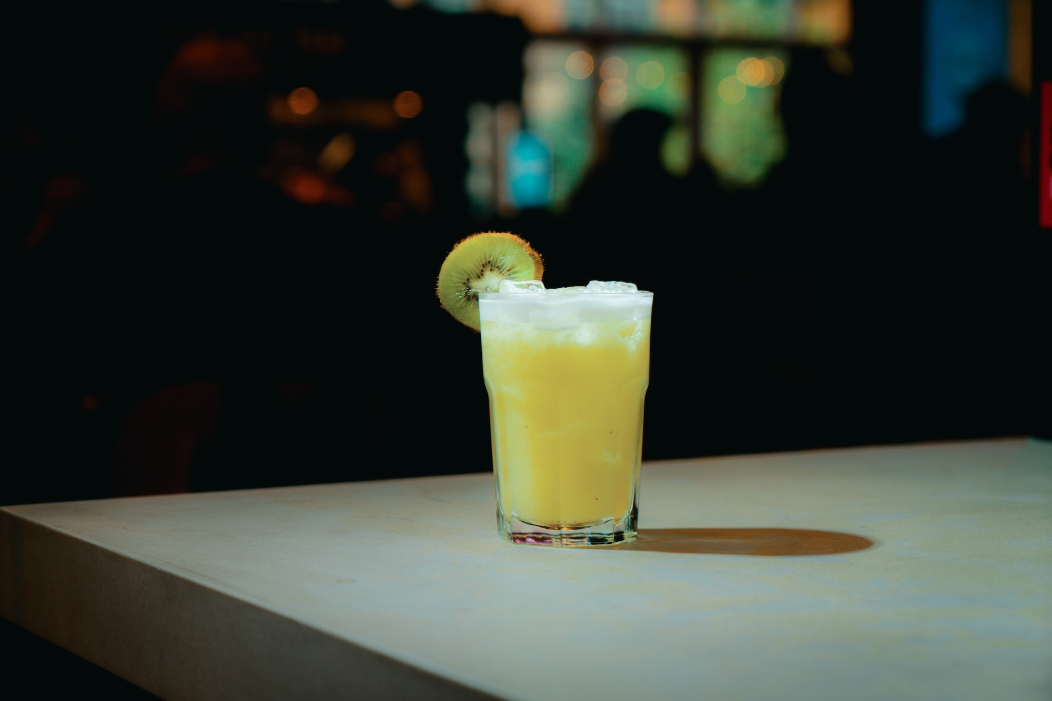 A greenish yellow cocktail with a kiwi on the glass