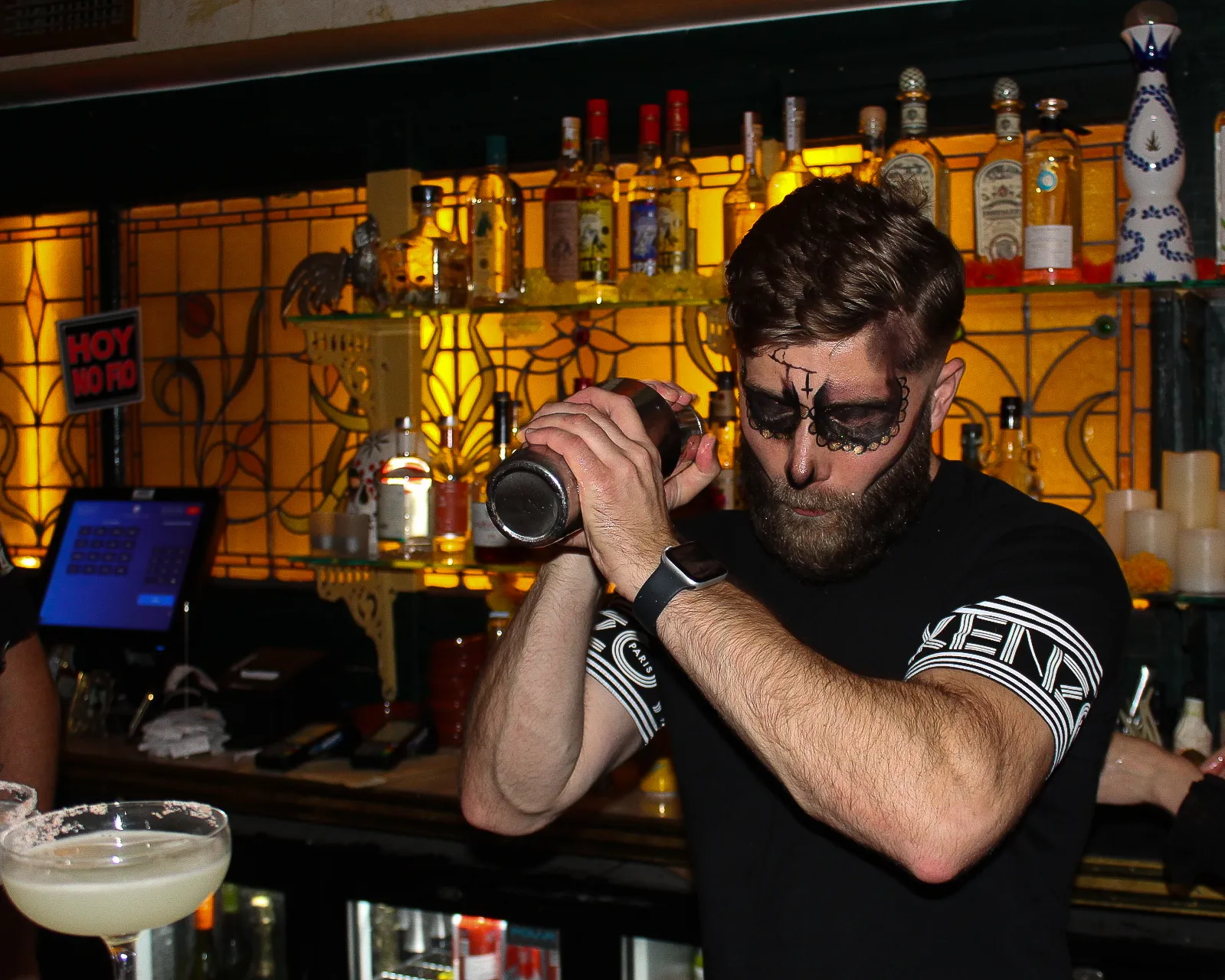 Bar tender with Day of the Dead face paint shaking a cocktail
