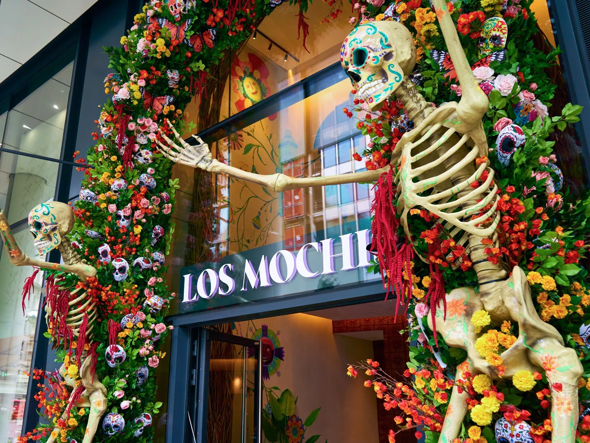 Giant skeletons stand at either side of a door decorated with a flower arch at Los Mochis Day of the Dead celebration