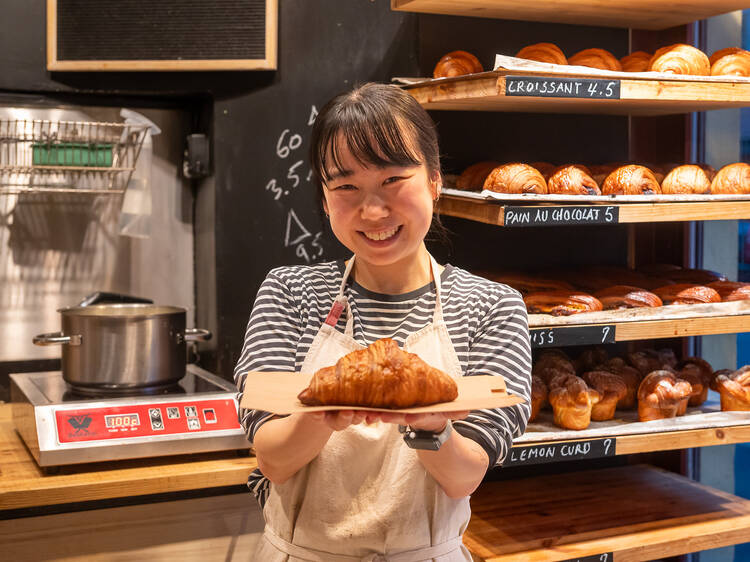 Tarjoilija ojentaa croissantia asiakasta kohden leipomossa Layers Bakery Helsingin Töölössä Tarjoilija ojentaa croissantia asiakasta kohden leipomossa Layers Bakery Helsingin Töölössä