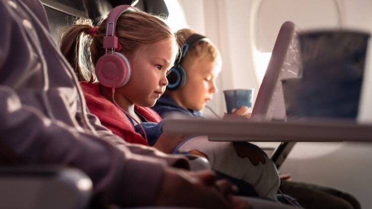 Family-friendly tips for flying with kids- Kids being entertained with gadgets while flying in airplane