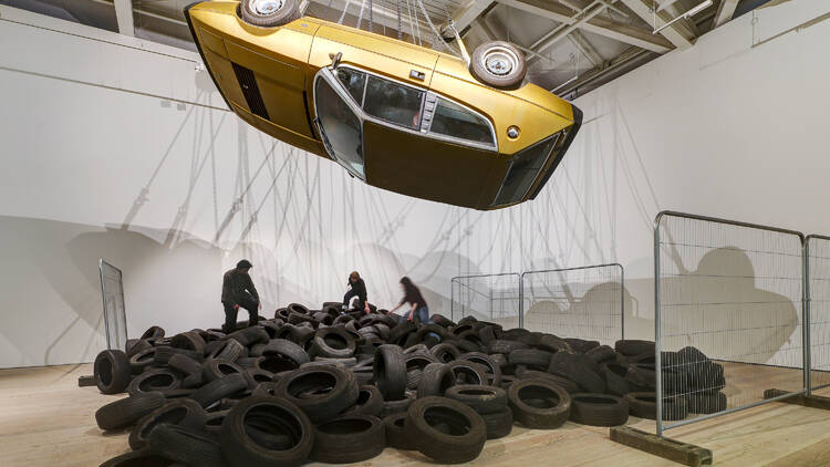 Yellow taxi suspended upside down over a pile of tyres 