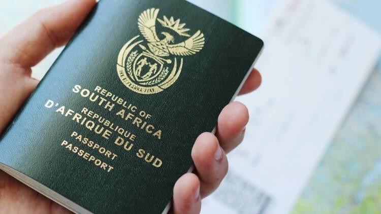 A South African travel passport in a man's hand with a plane ticket and map in the background A South African travel passport in a man's hand with a plane ticket and map in the background
