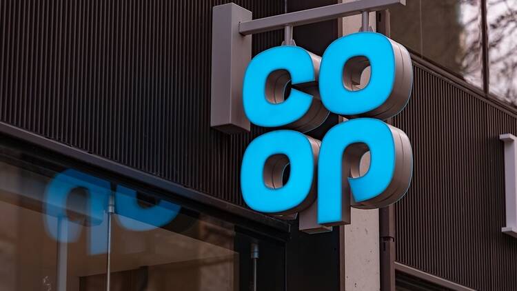 Photo of an illuminated blue sign hanging from a shop that says 'Co Op'