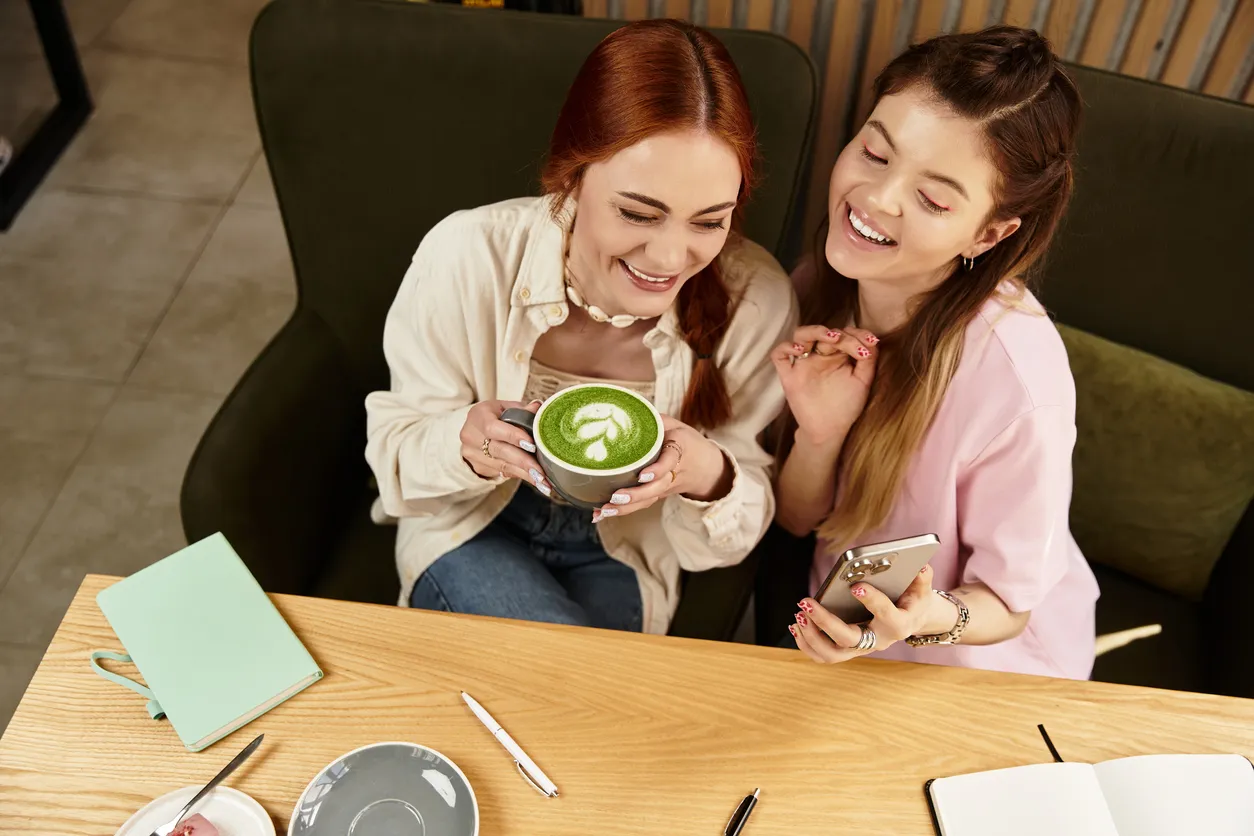 2222212802Two young women share a joyful moment at a chic cafe, smiling and enjoying their drinks together.