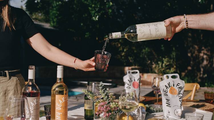A hand pours wine into a glass in a picnic setting. A hand pours wine into a glass in a picnic setting.
