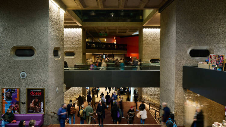 Photo of the inside of the Barbican with multiple walkways on different levels, concrete walls and lots of people in the hallways