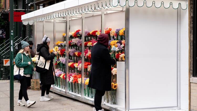 Three women look at felt flowers at a street-side shop.