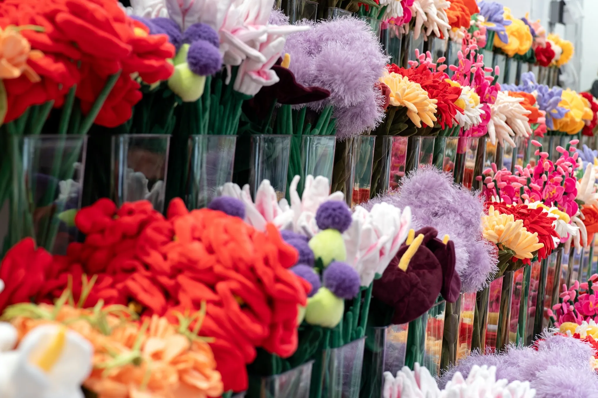 A line of vases is filled with colorful felt flowers.