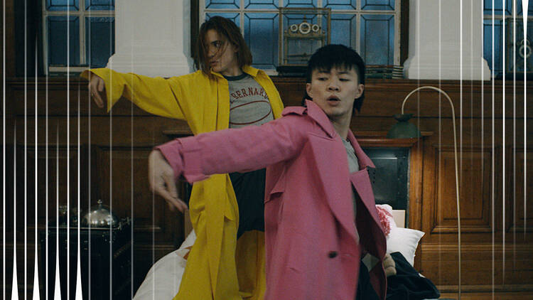Still from a dance film with two people dancing in pink and yellow trench coats Still from a dance film with two dancers in pink and yellow trench coats