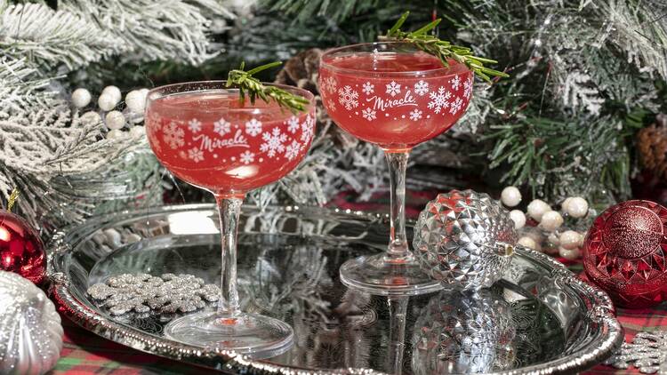 Miracle Bar Two red cocktails on a metal tray in front of christmas trees