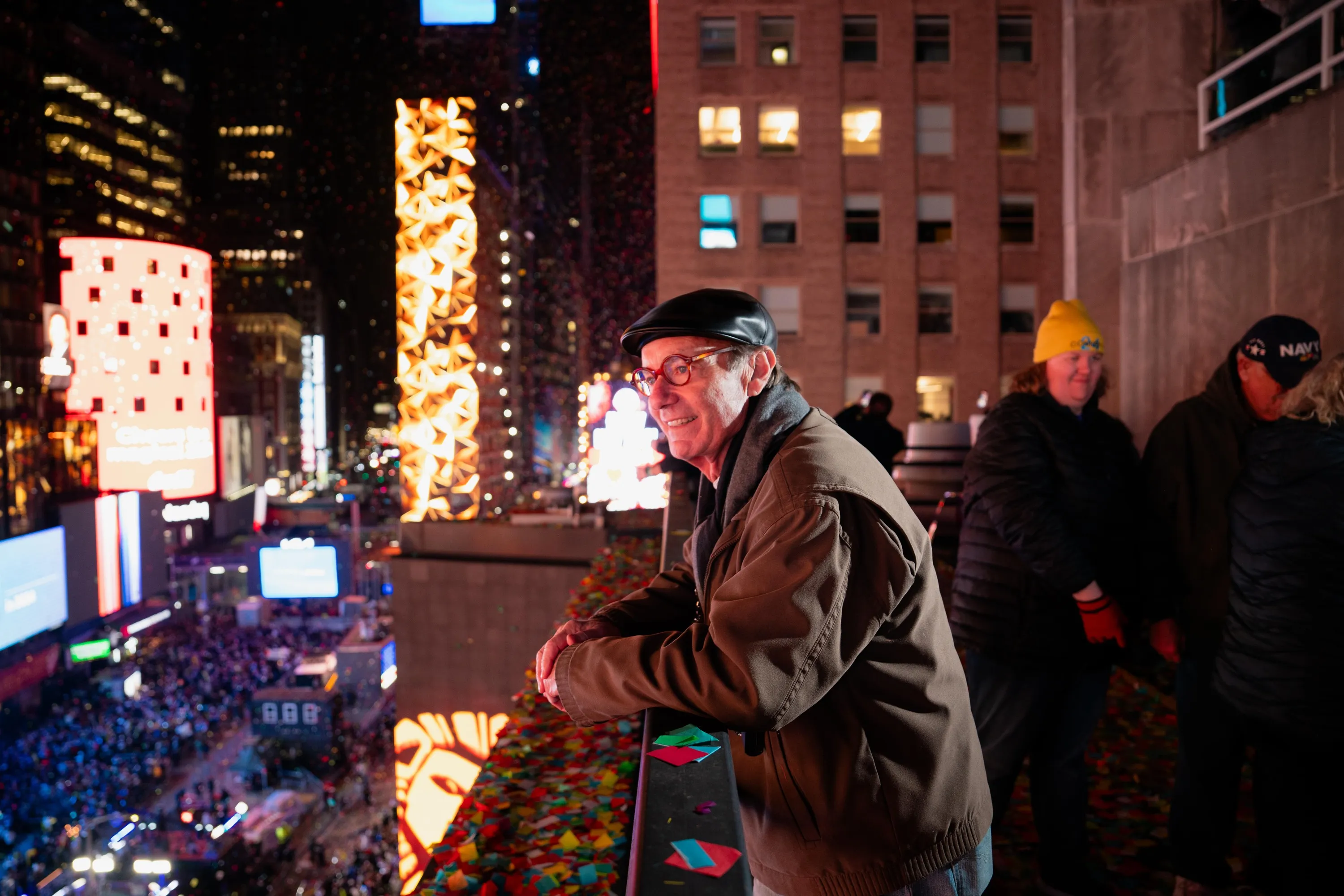 A man stands on a building above Times Square with confetti.