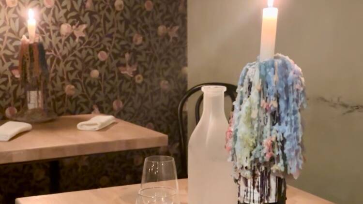 Tunnelmallinen ravintolapöytä Tampereen Apajassa, koristeltu sulaneilla värikynttilöillä, vesikarahvilla ja juomalaseilla.