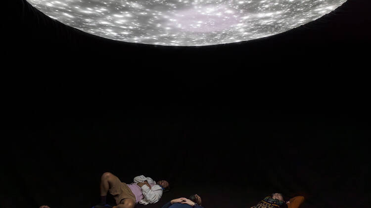 People lying beneath a glowy installation in art gallery