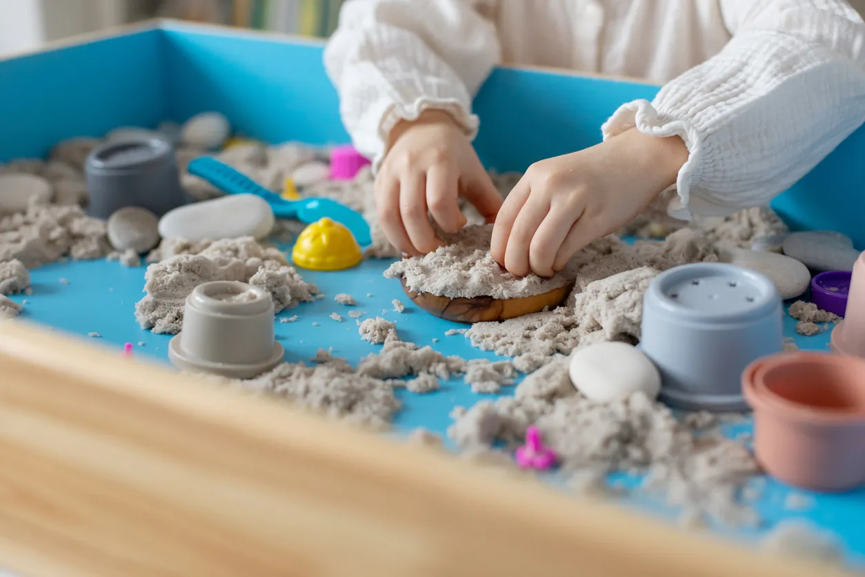 Toddler hands play therapy with colorful toys on sandbox.