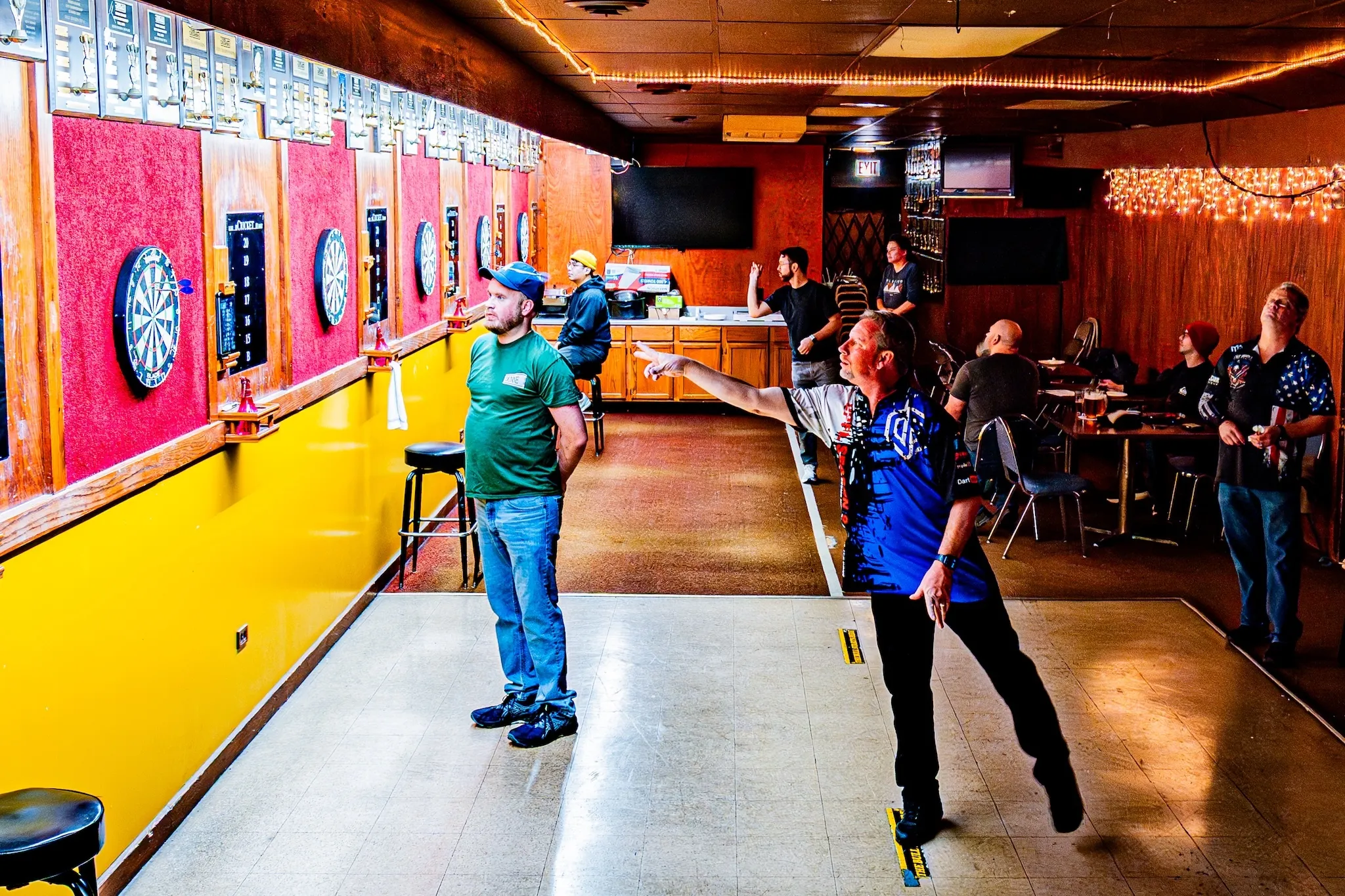 Patrons of Gamblers throw darts inside the dimly lit bar. 