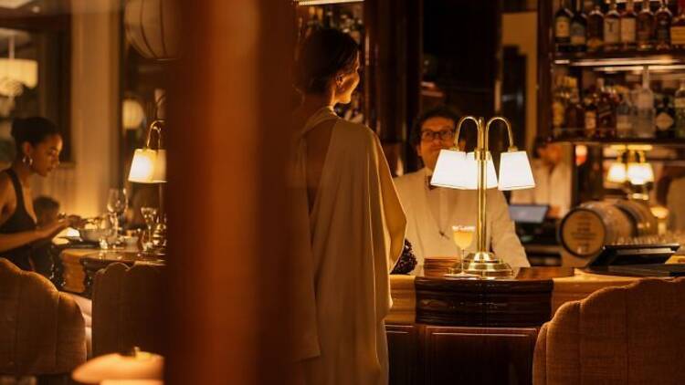 Tunnelmallisessa valossa nainen tilaa drinkkiä Kämpin baarista.