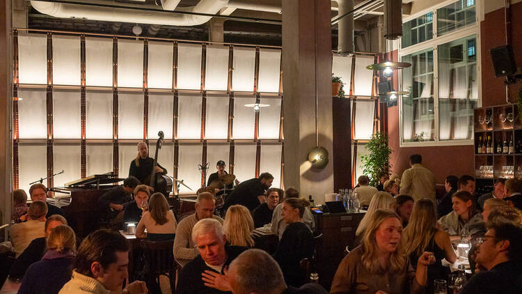 Ravintola Breran sali on täynnä ihmisiä syömässä, taustalla soittaa jazzbändi