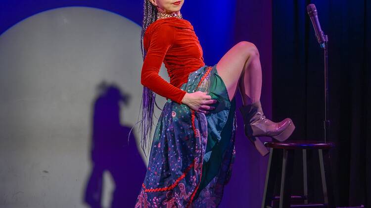 A woman performing on stage poses with her foot up on a stool. A woman performing on stage poses with her foot up on a stool.