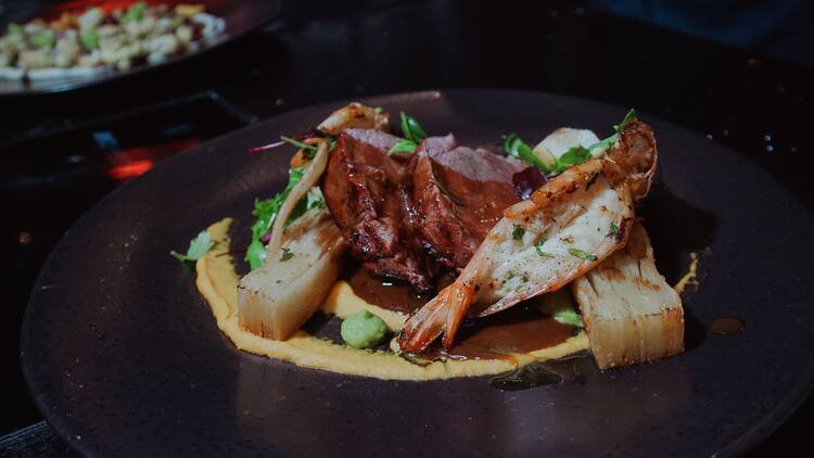La Cuna's surf & turf, featuring a tender beef fillet with tiger prawns, potato pavé, carrot purée, and garlic jus