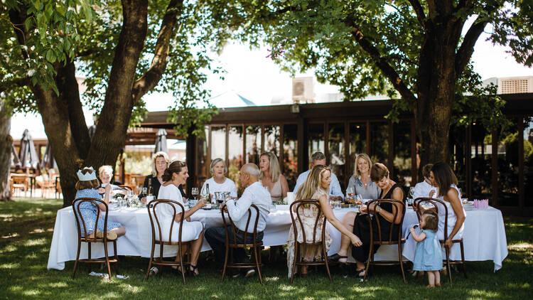 Brown Brothers People sitting at an outdoor table in a lush winery setting.