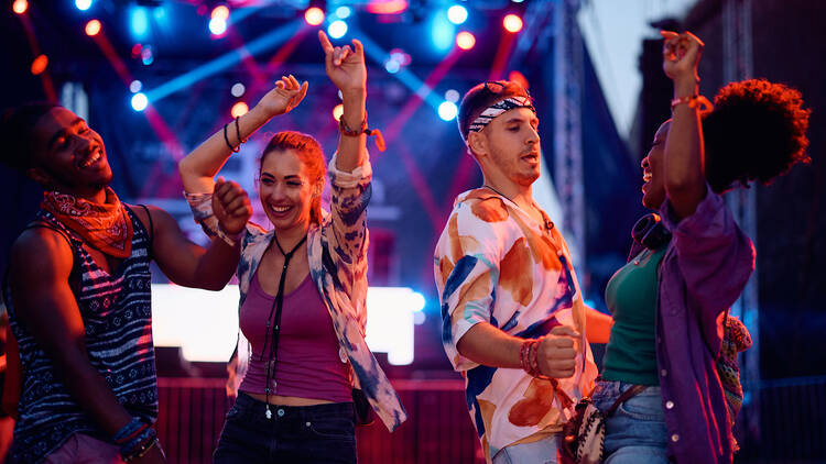 Young happy people dancing and having fun at summer music festival. 1567118111 Carefree festival goers dancing in front of the stage during open air music concert.