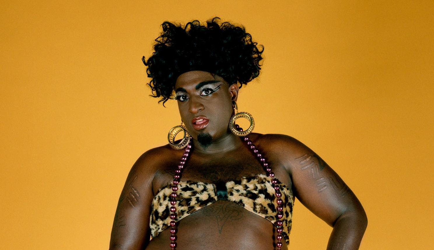 Portrait by Catherine Opie of a Black man in drag wearing a leopard print bikini in front of a yellow backdrop