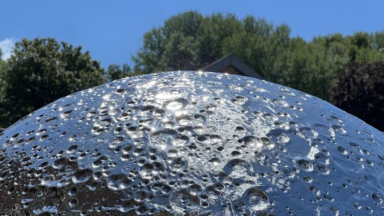 Photo of a silver shiny orb with lots of craters in outside reflecting the sun