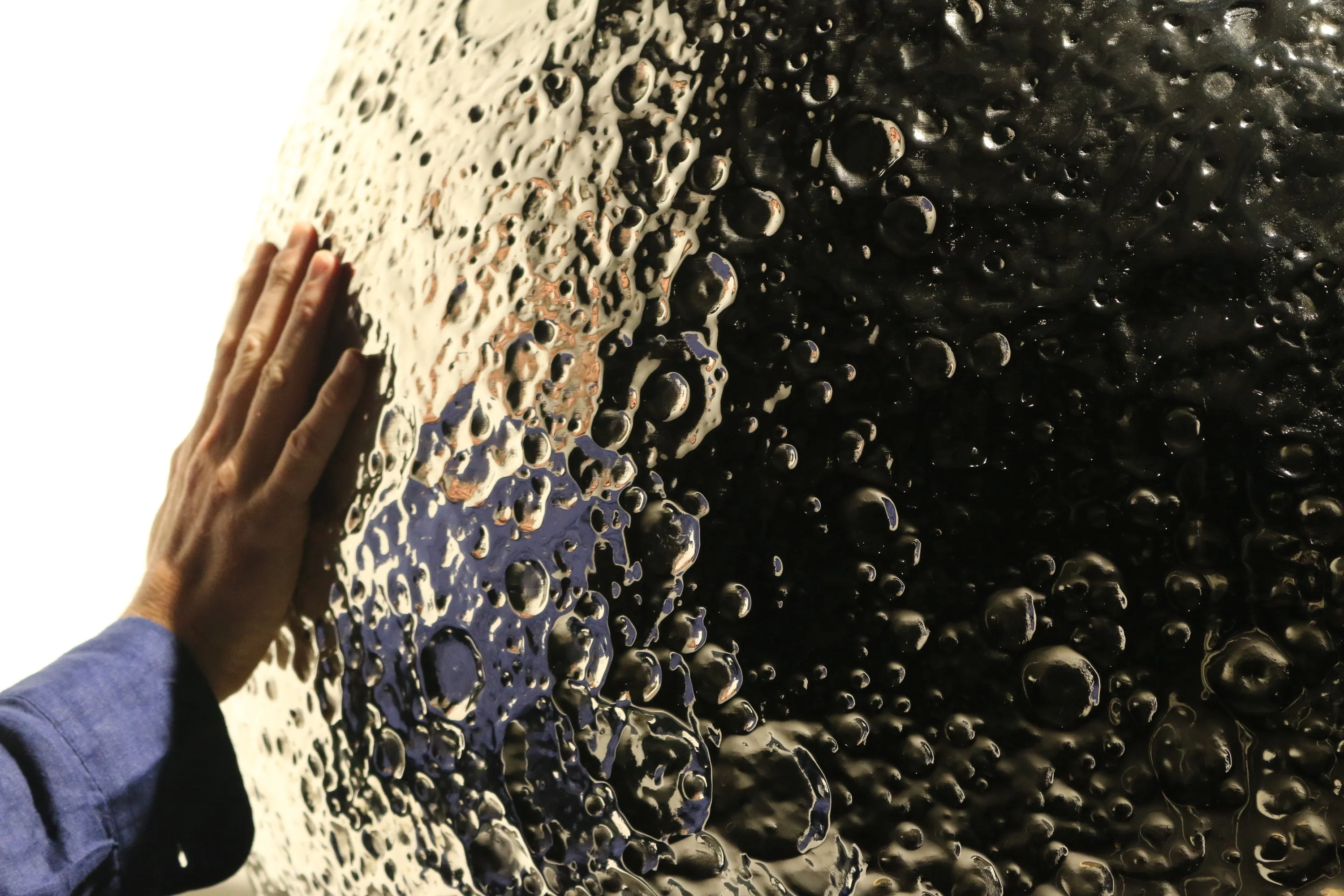 Photo of a man's hand touching a silver sphere replica of the moon with lots of craters and dips in