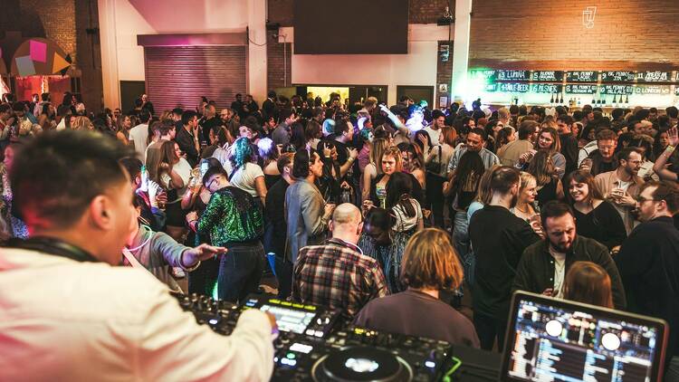Crowds dancing as a DJ plays music on decks and a laptop at Blackhorse Beer Mile party at Big Penny Social