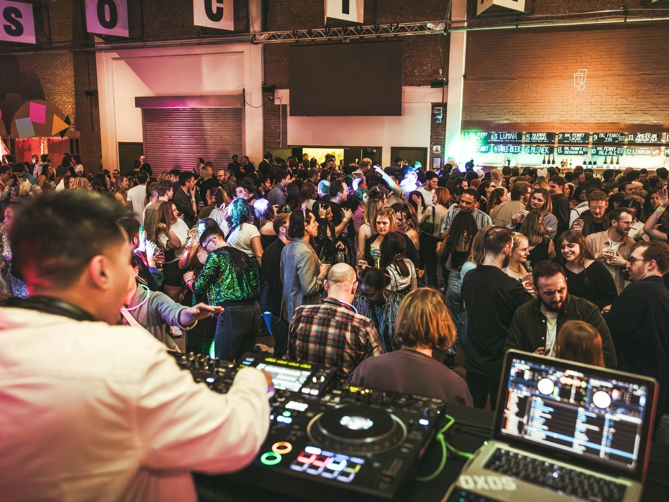 Crowds dancing as a DJ plays music on decks and a laptop at Blackhorse Beer Mile party at Big Penny Social