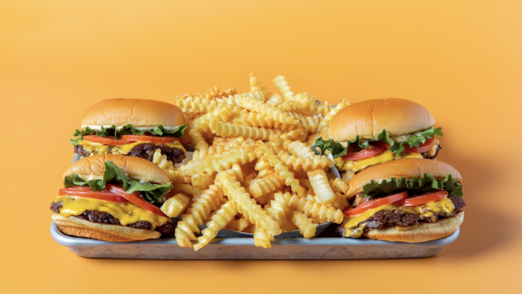 Photo of four beef cheeseburgers and lots of fries on a tray against a yellow background Photo of four beef cheeseburgers and lots of fries on a tray against a yellow background