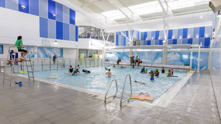 Photo of a small shallow indoor training swimming pool with families in it and a life guard 