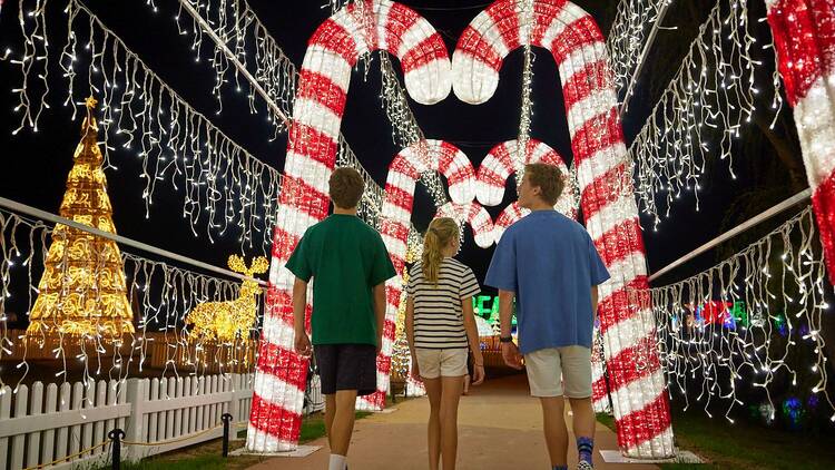 Three children walking through Christmas lights.