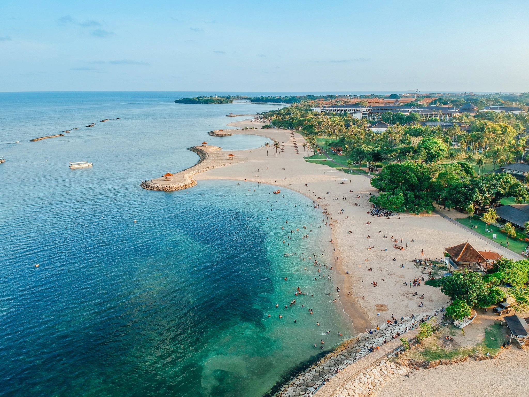 Aerial drone view of Holiday In Sanur Beach, Bali, Indonesia with ocean, boats, beach, villas, and people.