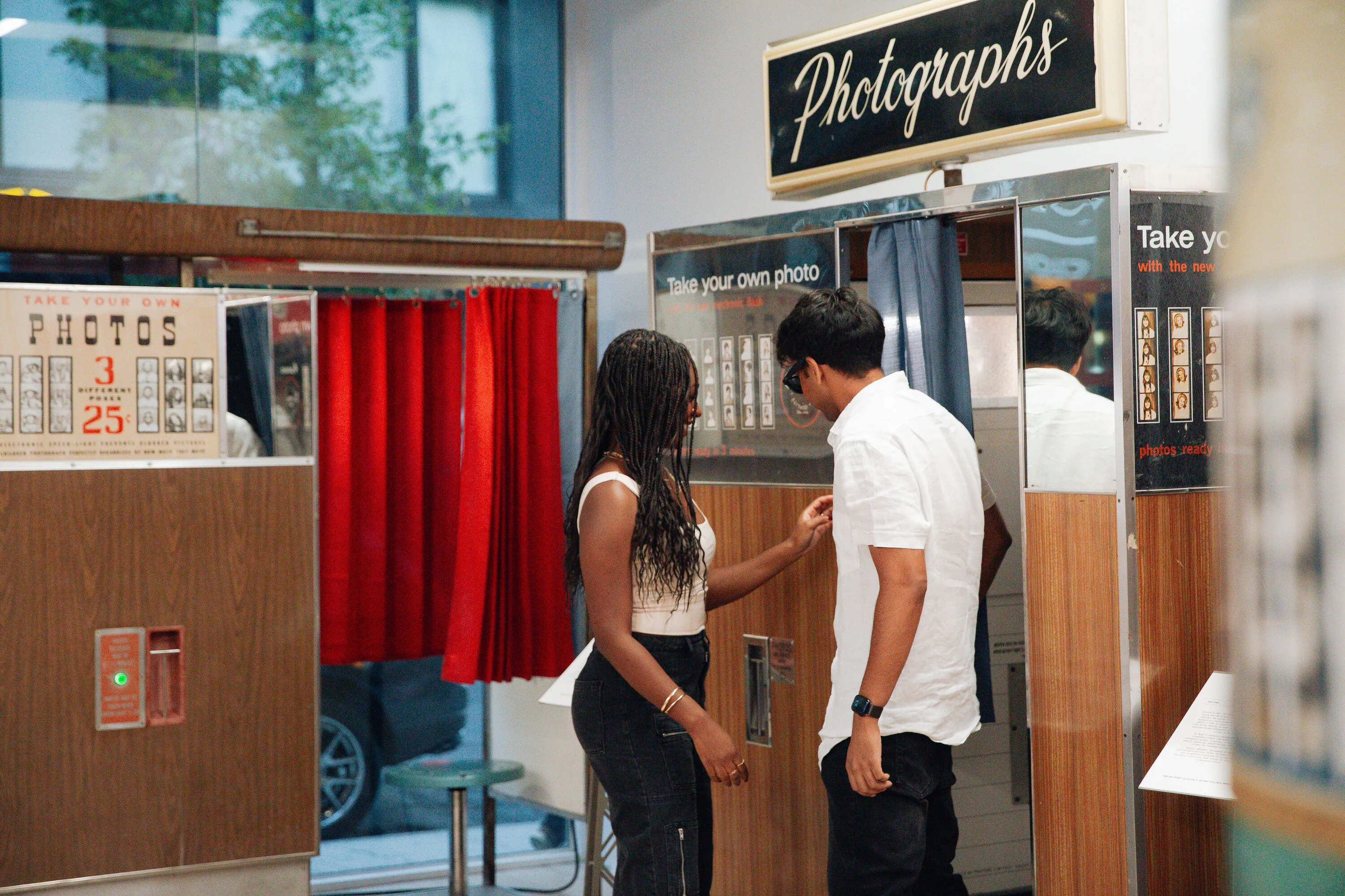 Two people step inside of a photobooth.