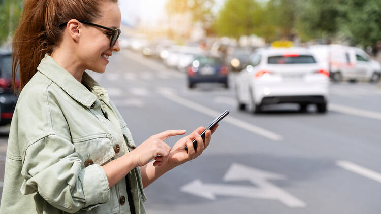 Urban woman using her smartphone while standing next to city road. 2152006200