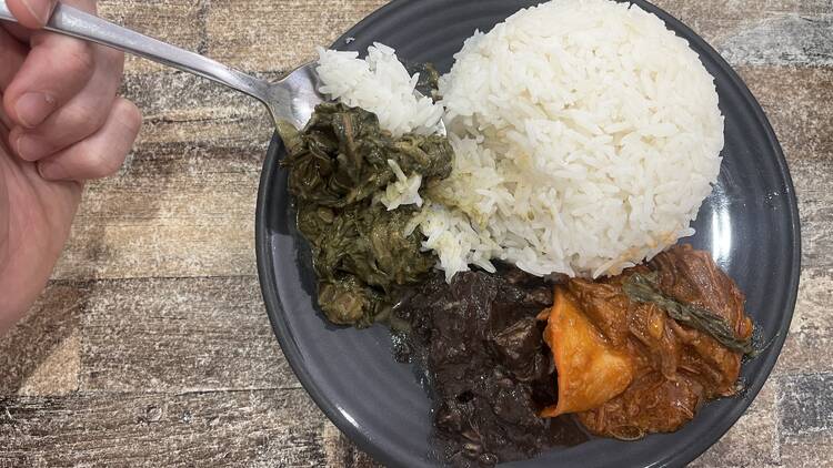 The Kamayan - Filipino A hand holding a fork eating rice and stew