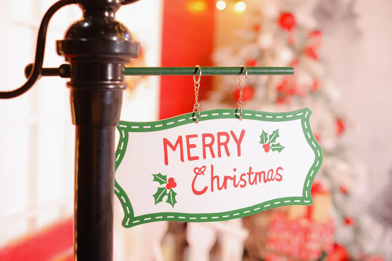 A sign attached to a post saying merry christmas time next to a decorated christmas tree