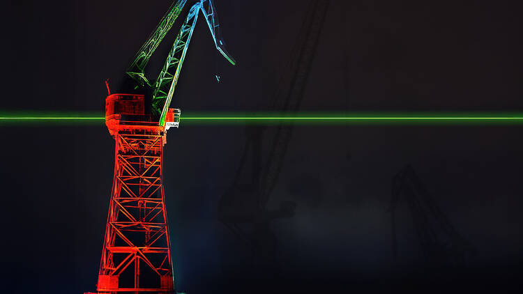 Valolla punaiseksi värjätty nostokurki, jonka läpi menee vihreä laserviiva