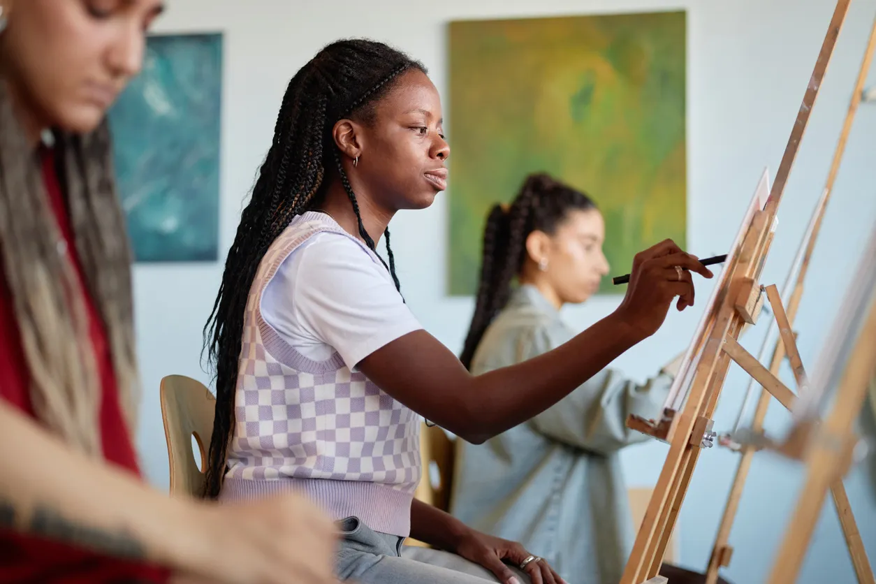 Young Black Woman Painting on Canvas during Art Class with Diverse Group