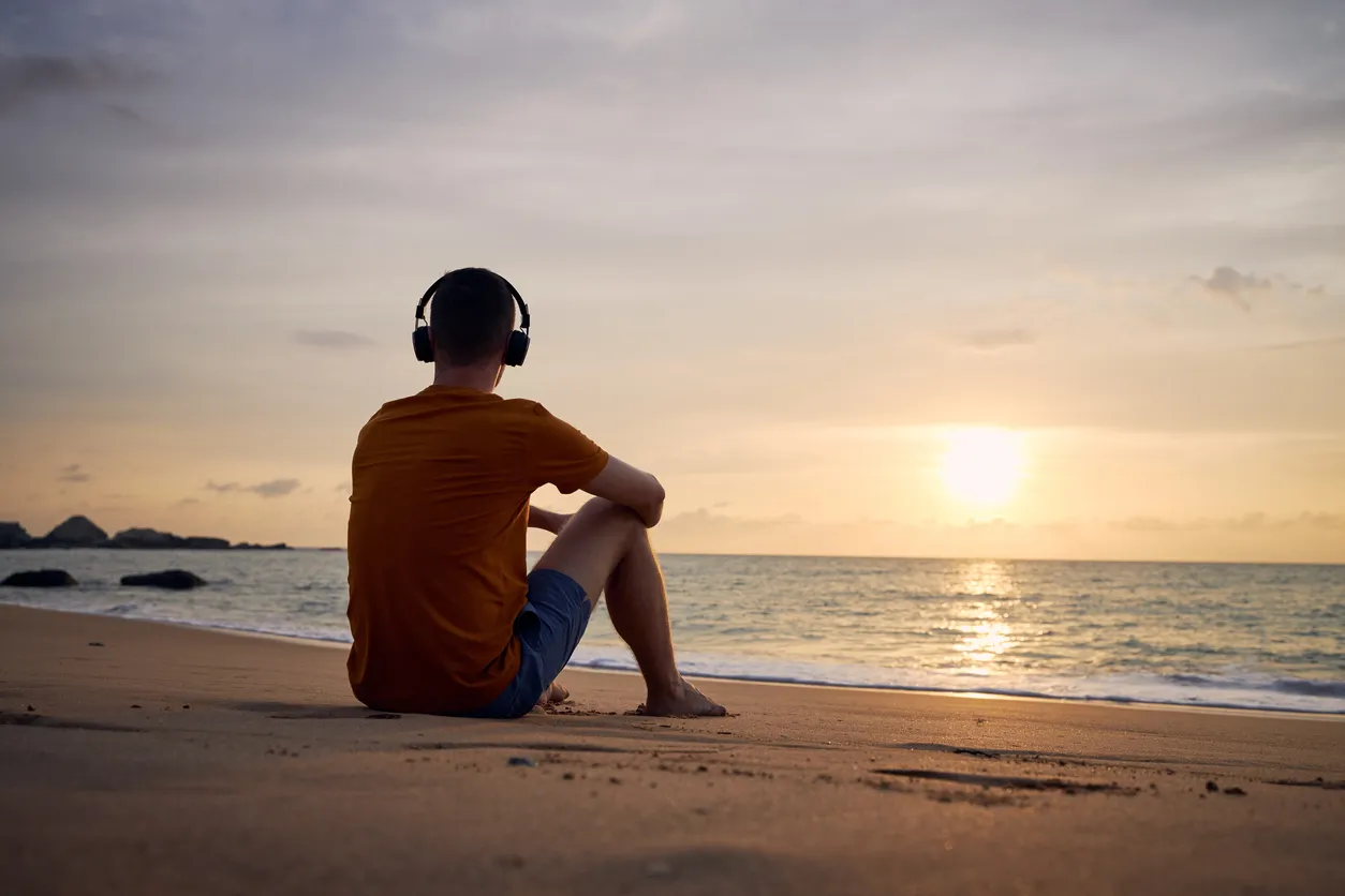 Rear view of man with headphones on beach. Serenity, contemplation and listening music at beautiful sunset."n