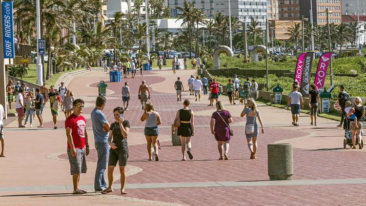 Many Unknown people walking on early morning  beachfront paved promenade against city skyline in Durban, South Africa