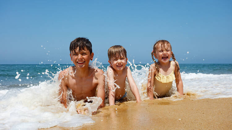 Laughing children crawling on the beach with the sea in the background, foamy waves splashing around, kids scream of excitement