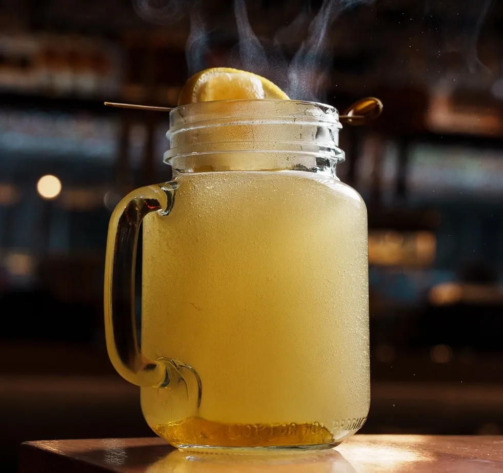 A yellow drink in a mug with a lemon wedge