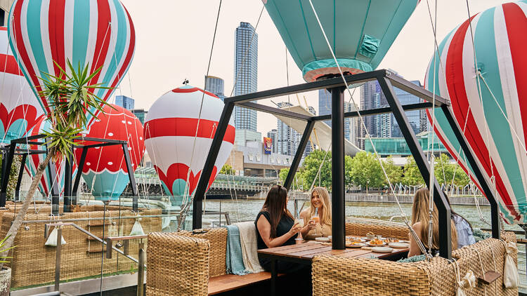The Wharf Hotel Group of women sitting at a hot air balloon-themed dining pod alongside the Yarra River.